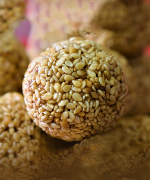 Plate of golden-brown Til ke Ladoo (Sesame Seed Ladoo), featuring their round shape and specks of sesame seeds, a delectable and traditional Pakistani sweet treat.